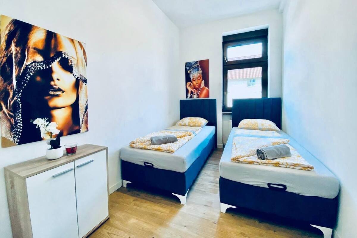 Une petite chambre moderne avec deux lits simples, une petite armoire blanche et un grand tableau au mur.