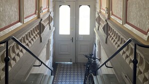 A grand staircase with ornate railings and a chandelier, leading to a set of double doors.