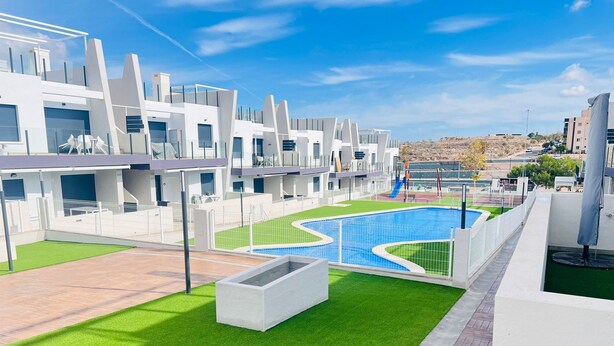 A modern apartment complex with a swimming pool, green lawns, and a view of the surrounding area.