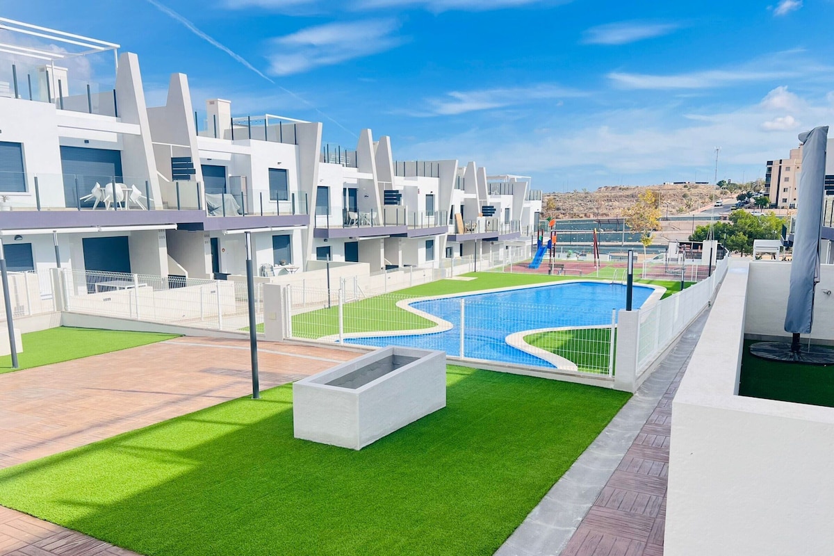 A modern apartment complex with a swimming pool, green lawns, and a view of the surrounding area.
