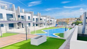 A modern residential complex with a swimming pool, green lawns, and white buildings.