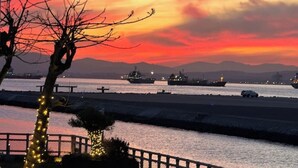 A sunset view with ships on the water, a dock, and a tree with lights.
