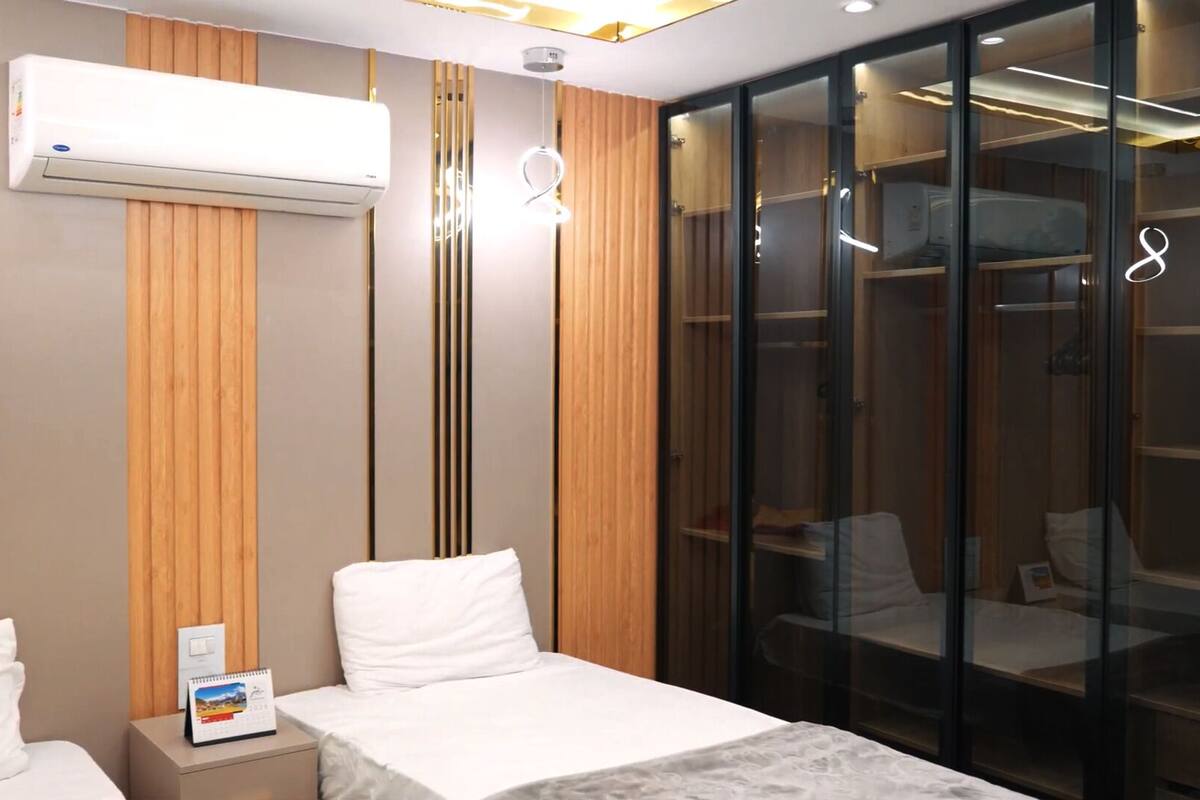 A hotel room with two beds, a wardrobe, and an air conditioning unit.