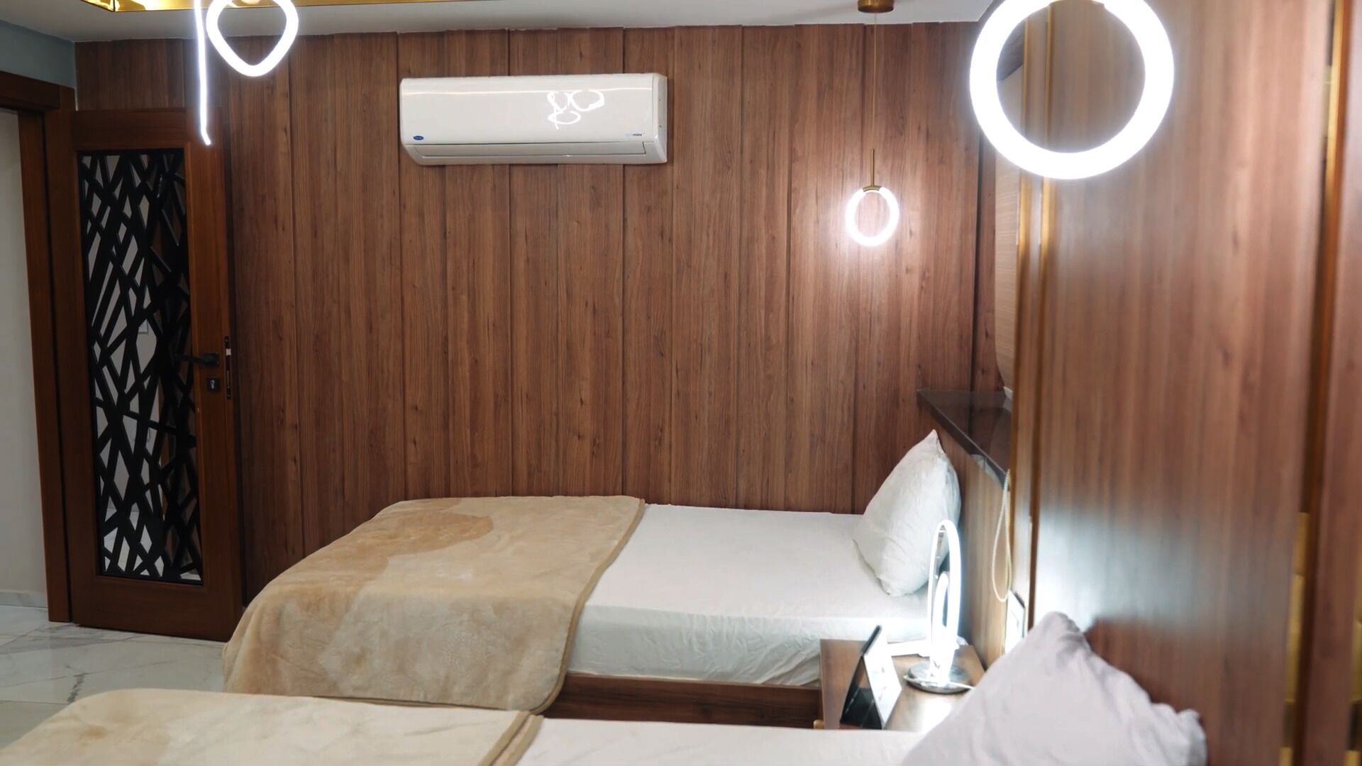 A hotel room with two beds, a wooden wall paneling, an air conditioning unit, and a decorative door.