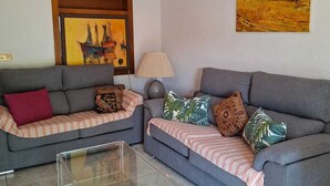 A living room with two grey sofas, a glass coffee table, a ceiling fan, a framed painting, and a landscape painting. - Fantastic apartment in La Manga Club. Swimming pool, restaurants, pubs, golf beach (Cartagena)
