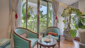 Una habitación con dos sillones color turquesa, una mesita redonda con un plato y dos tazas blancas, y una planta grande en maceta.