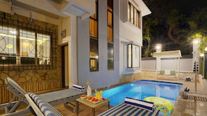 Zona junto a la piscina con sillones de descanso, una mesa con comida y bebidas, y una piscina pequeña.