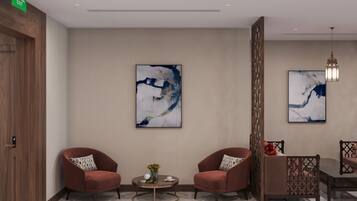 A modern lobby with two red armchairs, a round coffee table, and abstract paintings on the walls.
