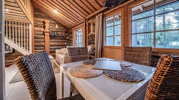 Ein rustikaler Innenraum einer Blockhütte, mit einem Essbereich, der Korbstühle und einen Tisch mit Untersetzern zeigt.