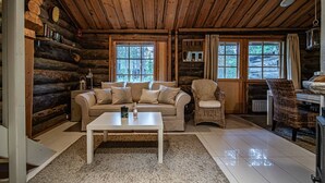 Ein gemütliches Blockhaus-Interieur mit einer Couch, Sesseln, einem Couchtisch und einem Kamin.