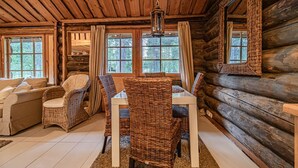 Ein Holzblockhaus-Interieur mit Essbereich, Korbmöbeln und großen Fenstern.