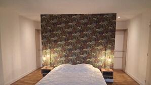 A bedroom with a large bed, a patterned wallpaper, and two bedside lamps. - Maison breronne (Meillac)