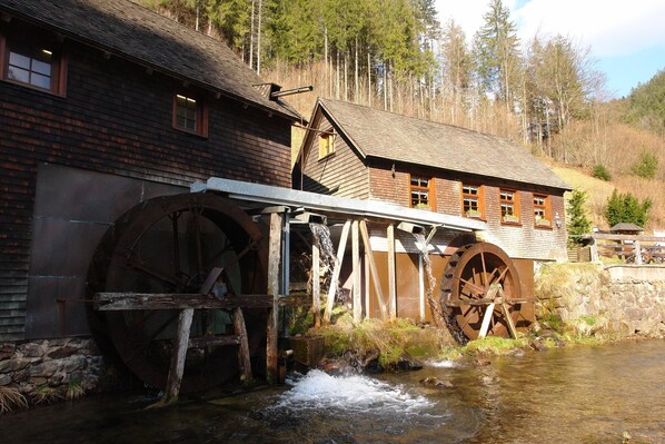 Un bâtiment rustique en bois, doté de grandes roues à eau et bordé par un ruisseau qui le longe.