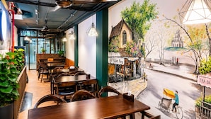 A restaurant interior with wooden tables and chairs, a mural depicting a street scene, and hanging pendant lights.
