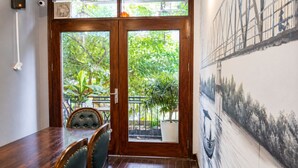 A dining area with a wooden table and chairs, a view of greenery outside, and a mural on the wall.