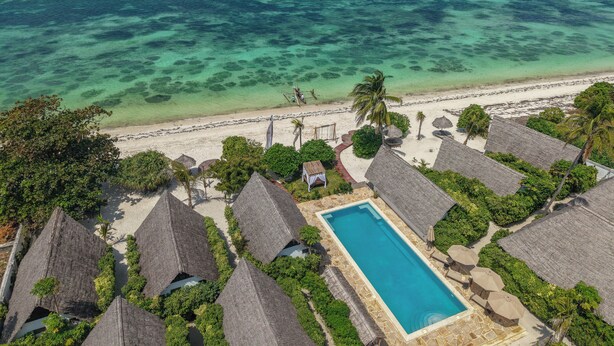 A resort with thatched-roof bungalows, a swimming pool, and a beach with clear turquoise waters.