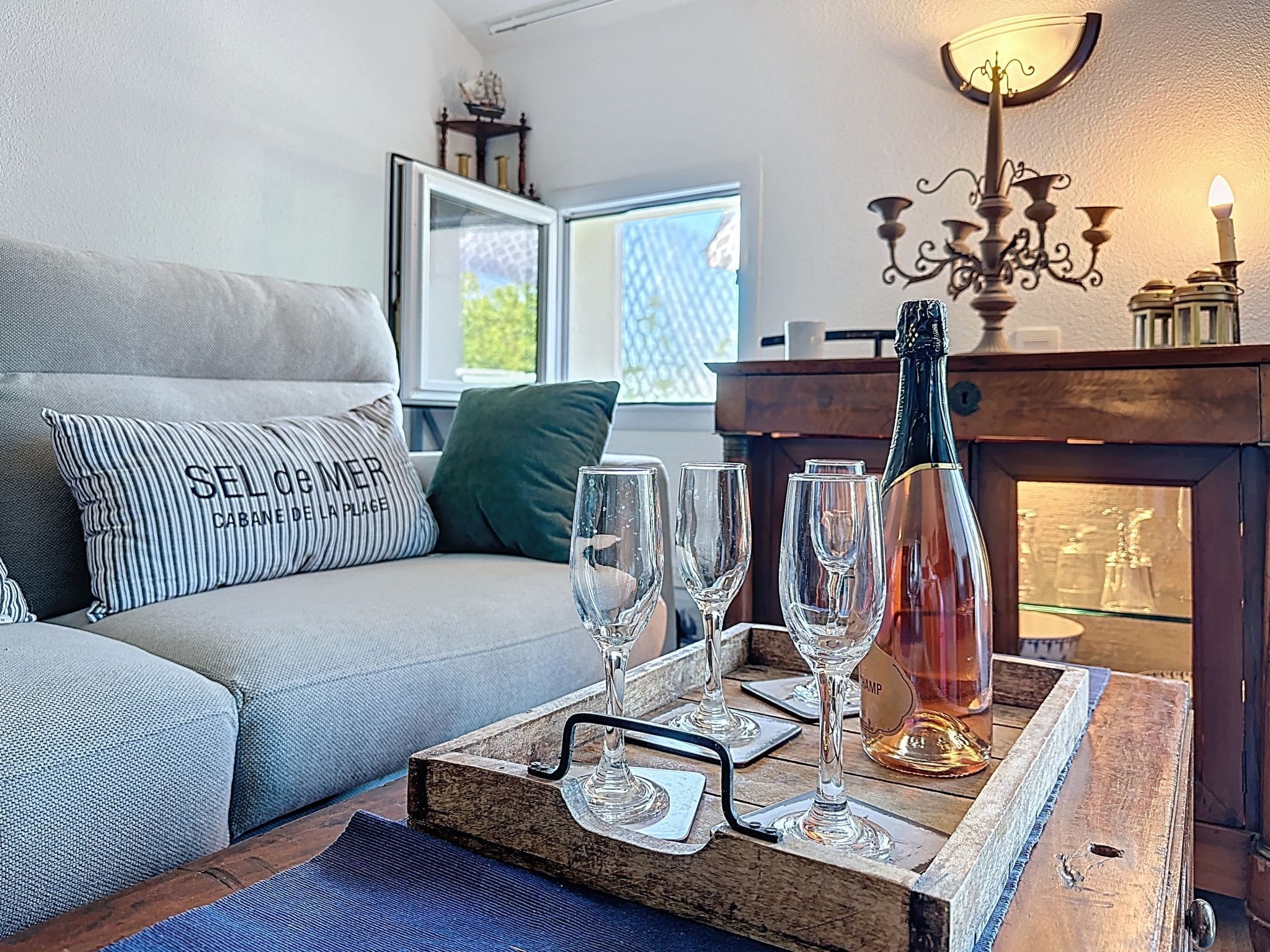 A cozy living room with a sofa, a wooden side table with glasses and a bottle, and a window with a view.