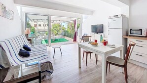 A modern living room with a sofa, a dining table, and a kitchen area with a refrigerator and a microwave.