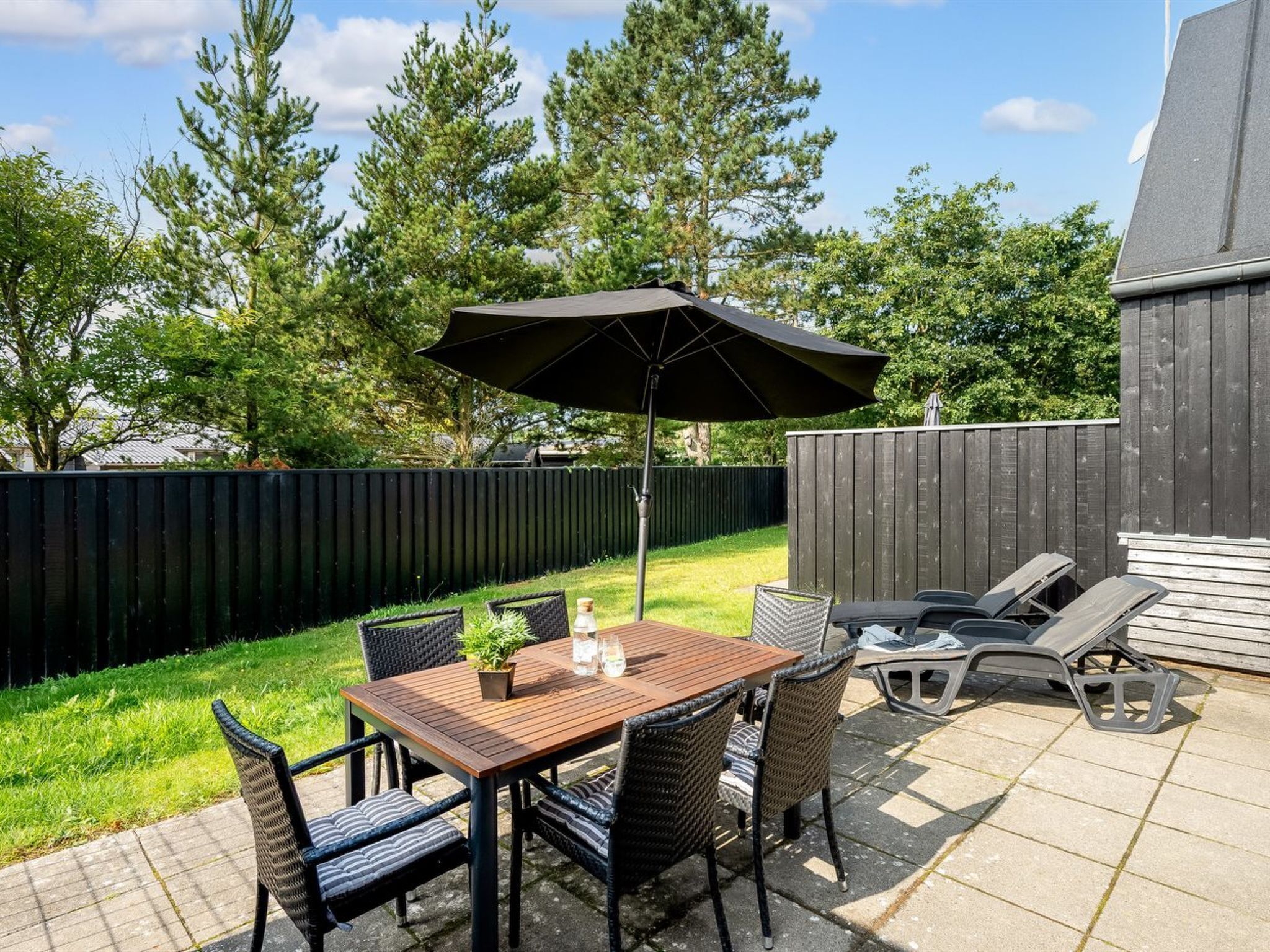 A patio with a table and chairs, an umbrella, and a wooden fence in the background.