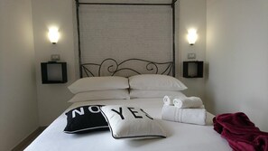 Ein ordentlich bezogenes Bett mit weißen Laken, einem schwarz-weißen Kopfkissen mit dem Aufdruck 'NO YES' und einer roten Decke.