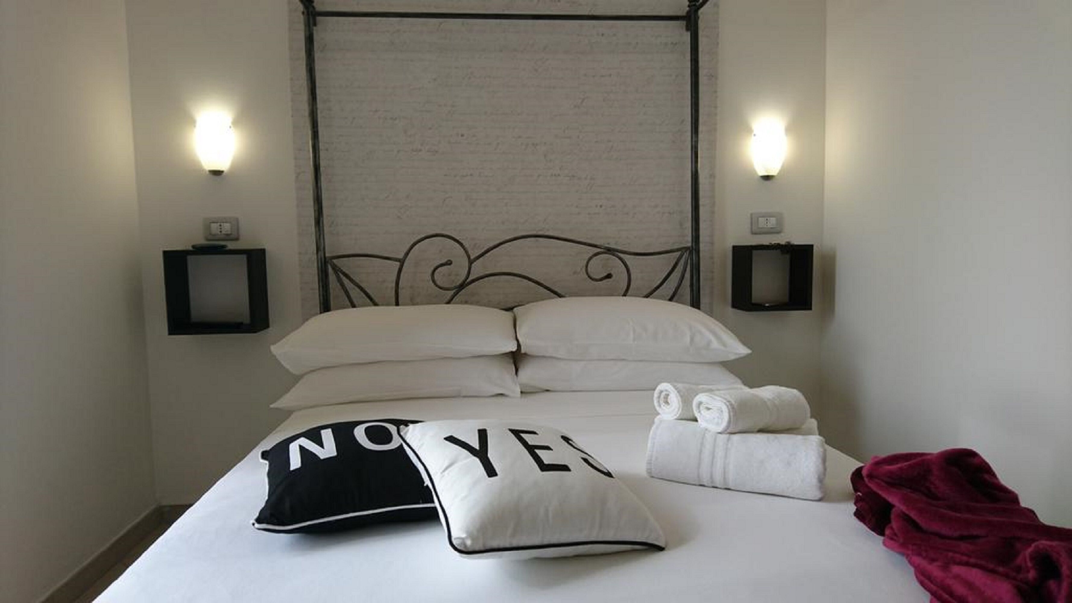 A neatly made bed with white linens, a black and white pillow with 'NO YES' text, and a red blanket.