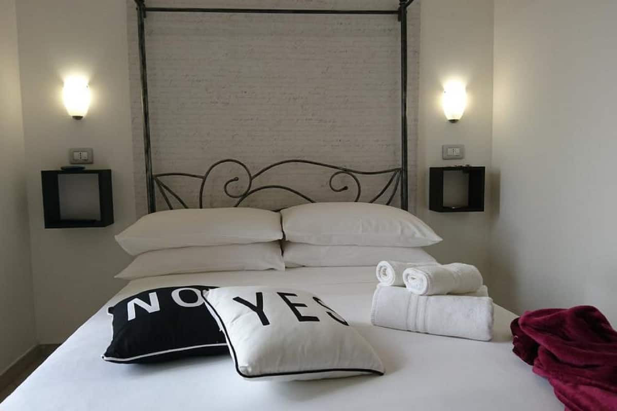 Un lit bien fait, avec du linge de lit blanc, un coussin noir et blanc orné du mot « NON » d’un côté et du mot « OUI » de l’autre, et une couverture rouge.
