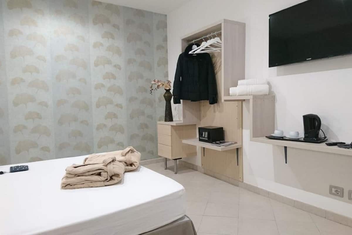 Une chambre d’hôtel comprenant un lit, un bureau avec un téléphone et une machine à café, une télévision, une armoire et une salle de bain avec un porte-serviettes.