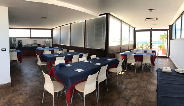 A conference room with tables set for meetings, large windows with blinds, and a kitchenette in the background. - Centrale (Syracuse)