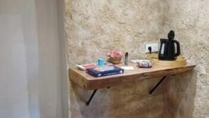 A small, narrow room with a slanted ceiling, a wooden shelf with various items, and a door. - Room in 15th-century castle tower (Mauvières)