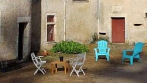 A courtyard with a stone building, a red door, and outdoor furniture including two blue chairs and a table. - Room in 15th-century castle tower (Mauvières)