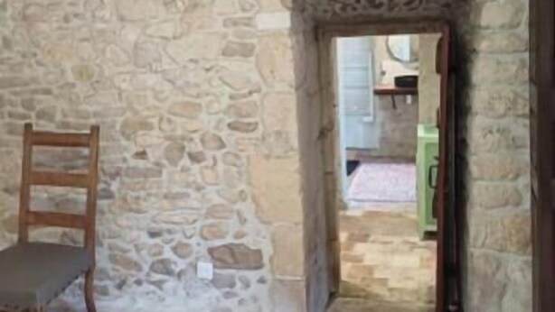 A stone-walled room with a wooden chair, a doorway leading to another room, and a wooden beam ceiling. - Room in 15th-century castle tower (Mauvières)
