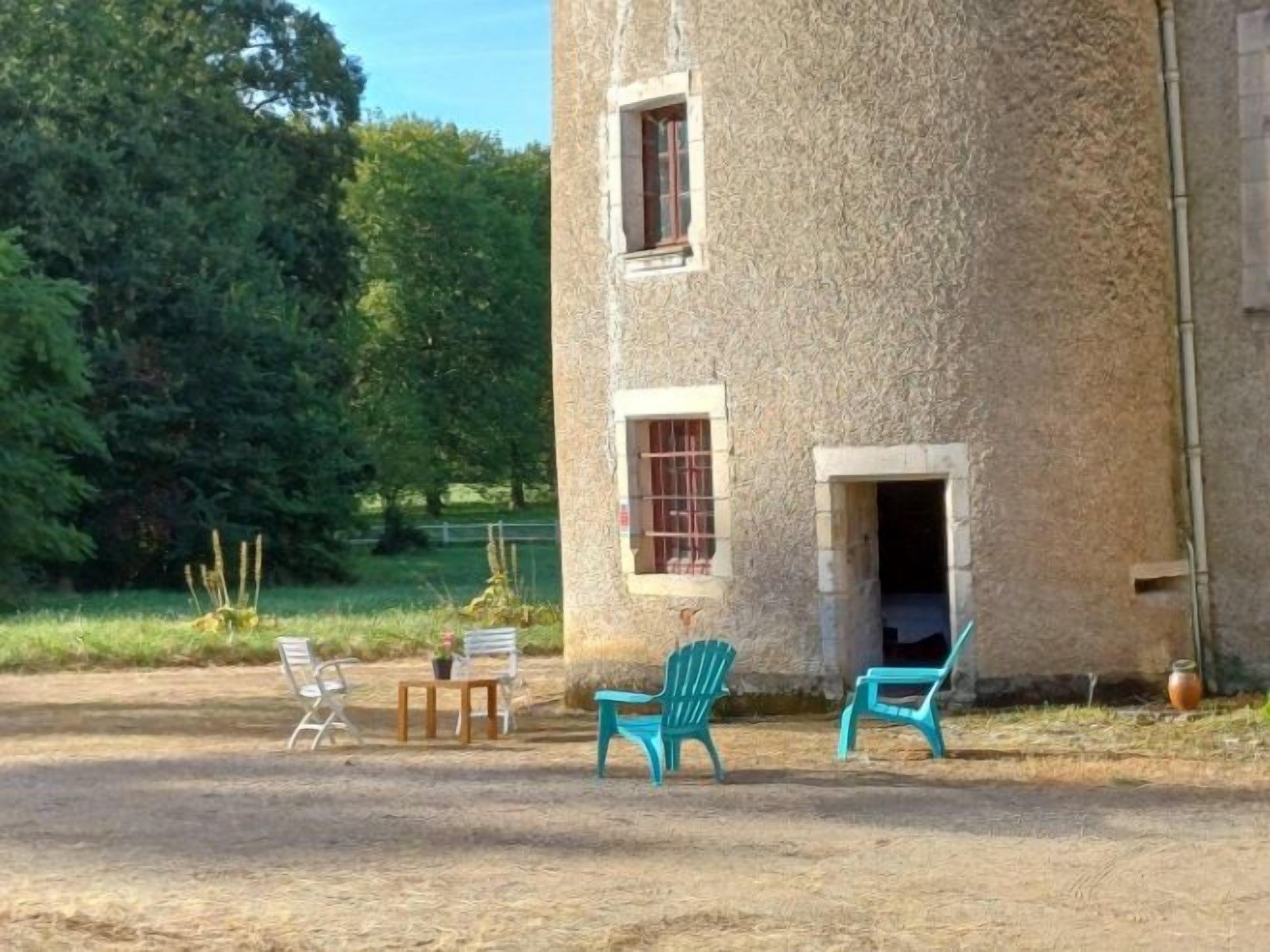Een landelijk stenen gebouw met een klein terras, voorzien van twee stoelen en een tafel.