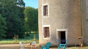A rustic stone building with a small porch area featuring two chairs and a table. - Room in 15th-century castle tower (Mauvières)