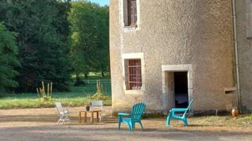 Een landelijk stenen gebouw met een klein terras, voorzien van twee stoelen en een tafel.