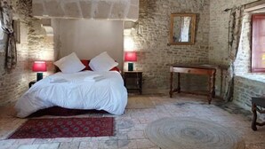 A rustic bedroom with a stone wall, a wooden bed, two bedside tables with lamps, and a small wooden table. - Room in 15th-century castle tower (Mauvières)