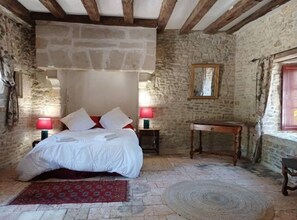 A rustic bedroom with a stone wall, a wooden bed, two bedside tables with lamps, and a small wooden table. - Room in 15th-century castle tower (Mauvières)