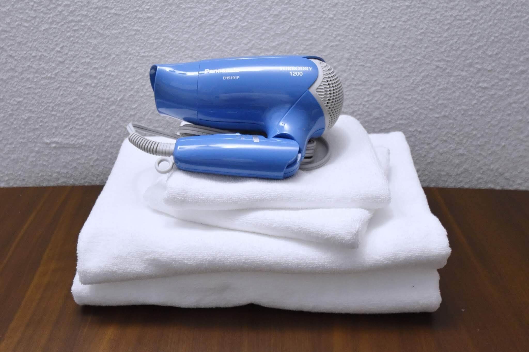 Un secador de pelo azul y su cable sobre una toalla blanca doblada en una mesa de madera.