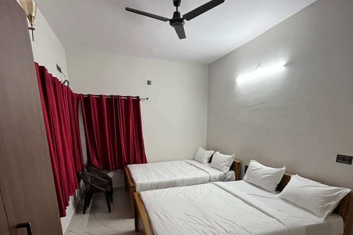 A room with two single beds, a ceiling fan, a desk with a chair, and red curtains.