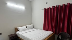 A bedroom with a bed, a nightstand, a chair, a ceiling fan, and a red curtain.