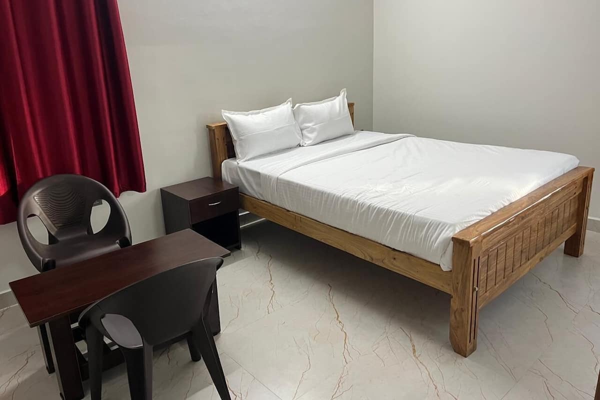 A bedroom with a wooden bed, white bedding, a desk with a chair, and a nightstand.
