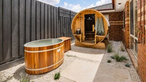 Un bain à remous en bois et un sauna se trouvent dans un jardin, avec un mur en briques et une clôture en bois.