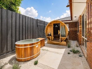 Un bain à remous en bois et un sauna se trouvent dans un jardin, avec un mur en briques et une clôture en bois.