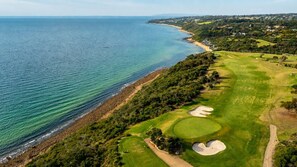 A coastal golf course with a clear view of the ocean, a sandy beach, and a well-maintained green area with sand bunkers. - Private Sauna + Ice Bath | Coastal Wellness Escape (Capel Sound)