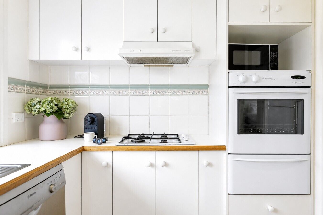 A kitchen with white cabinets, a microwave, an oven, a gas stove, and a coffee maker.