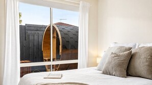 Une chambre avec un grand lit, des rideaux blancs et une vue sur une structure en bois à l’extérieur.