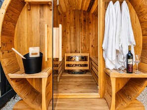 Eine Holzzimmer-Sauna mit einer Sitzbank, einem Eimer, einem Handtuch und einer Weinflasche.
