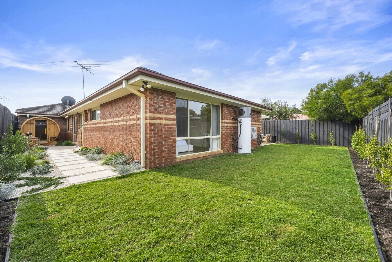 A single-story brick house with a large window, a satellite dish, and a fenced backyard.