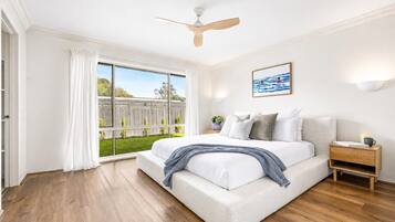 A bedroom with a bed, a ceiling fan, a nightstand, and a view of a garden through a sliding door.