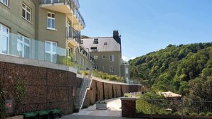 A residential building with a stone facade, a curved pathway, and a hillside in the background.