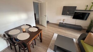 A modern living room with a dining area, a flat-screen TV mounted on the wall, and a potted plant. - Haus am Röblinsee - Stork vacation apartment in Fürstenberg / Havel (Fürstenberg/Havel)